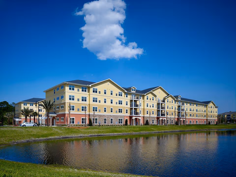 Four-story yellow and red residential building beside a pond under a blue sky