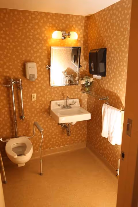 Compact bathroom with sink, mirror, towel rack, and a toilet in patterned walls.