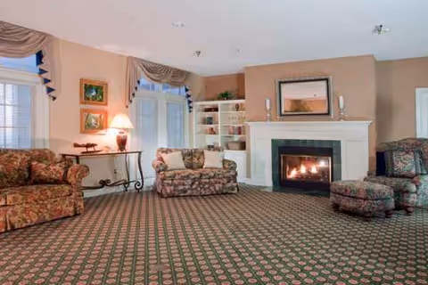 Cozy senior living lounge with floral sofas, a fireplace, and built in bookshelves.