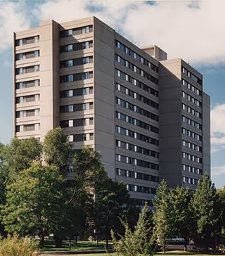 Exterior view of a multi-story apartment building surrounded by trees under a partly cloudy sky.