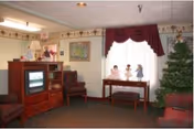 Cozy senior living lounge featuring a TV, chairs, a display table, and red curtains.