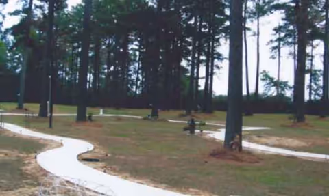 Winding white path curves through a grassy outdoor area with tall trees.