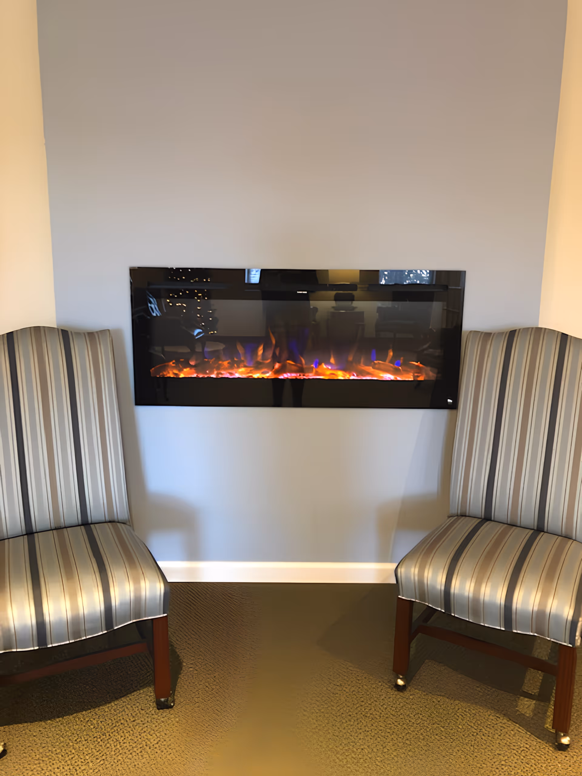 Two striped chairs flanking a wall-mounted electric fireplace in a seating area.