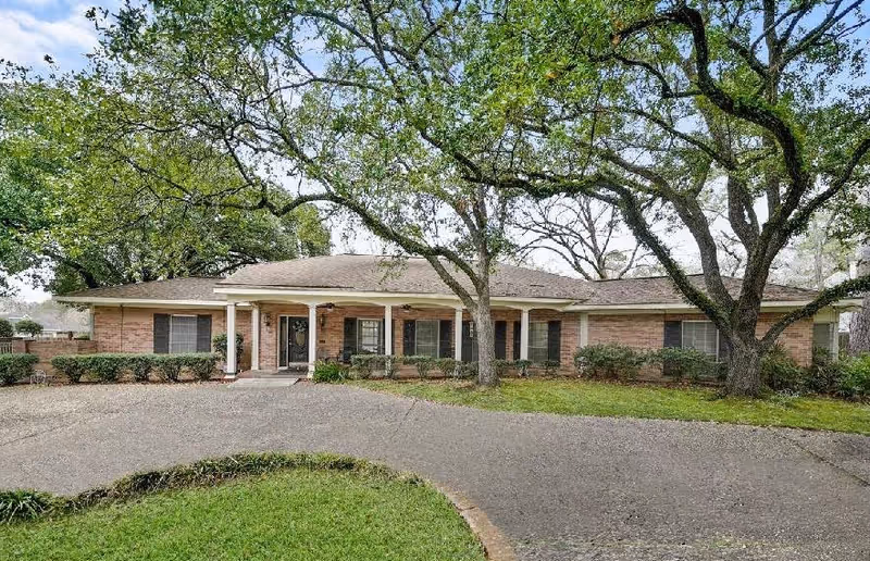Single-story brick residential building with a circular driveway and large trees in the front yard.
