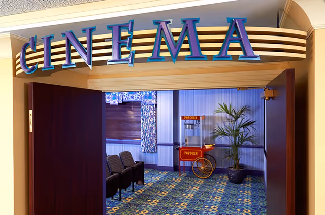 Entrance to a small cinema room with a popcorn cart, theater seats, and a large 'CINEMA' sign above the doorway.