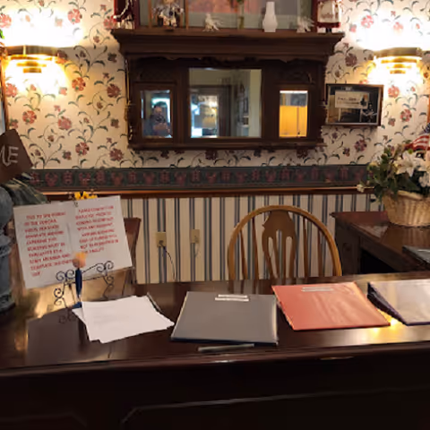 Wooden front desk in a floral wallpaper reception area with folders and a mirror