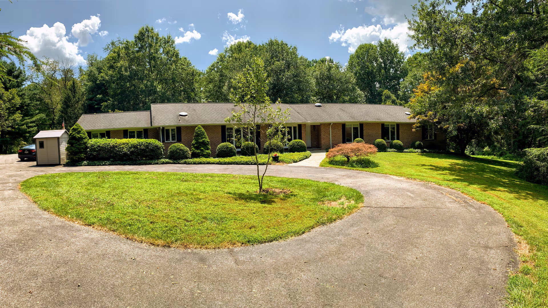 Single-story brick ranch-style building set behind a circular driveway with a manicured lawn and trees under a blue sky.