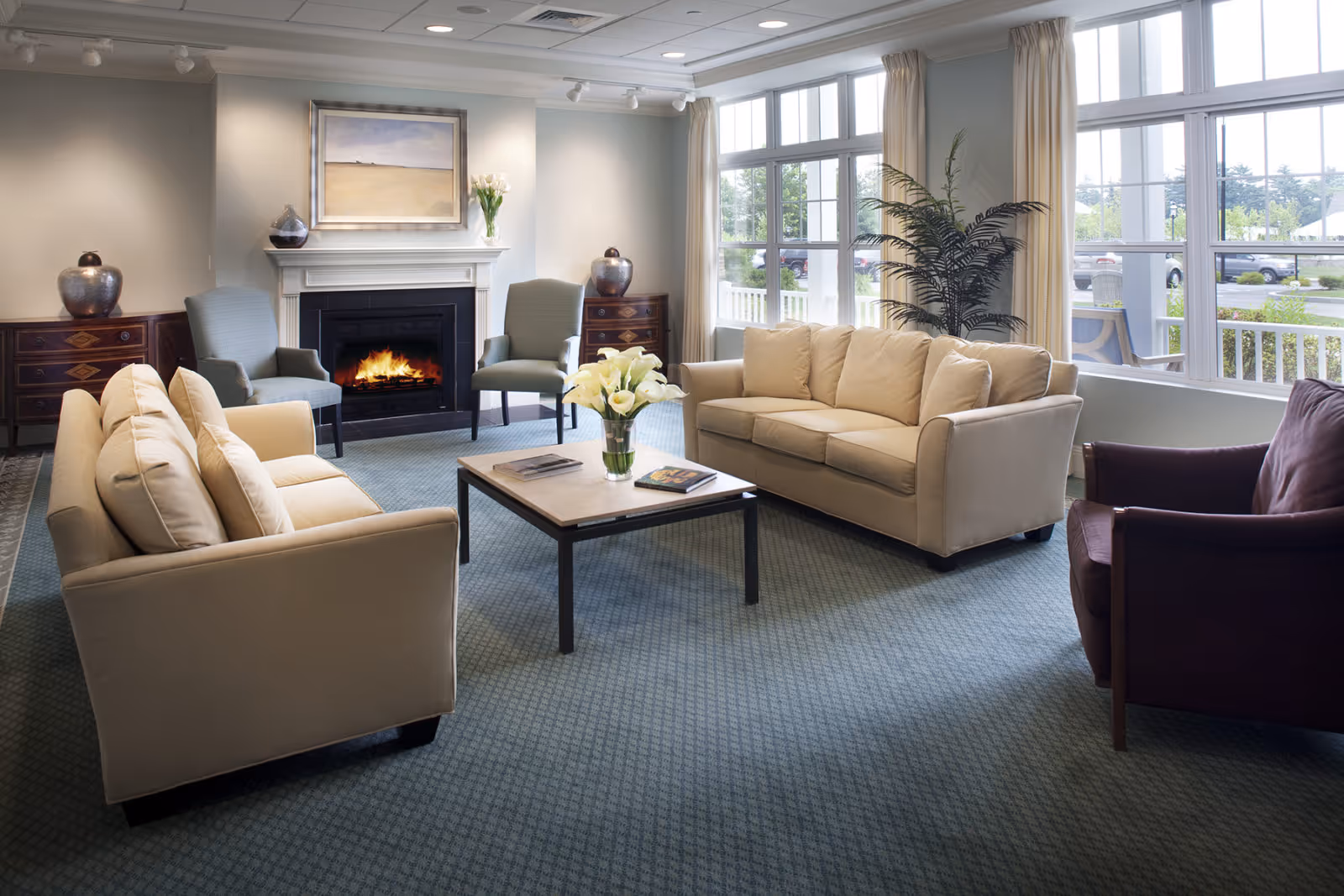Bright communal living room with sofas, armchairs, a coffee table, a fireplace and large windows overlooking the outside.