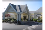 Front exterior view of Richmond Beach Rehab facility showing a covered entrance with columns, a driveway, landscaped bushes, and a clear sky.