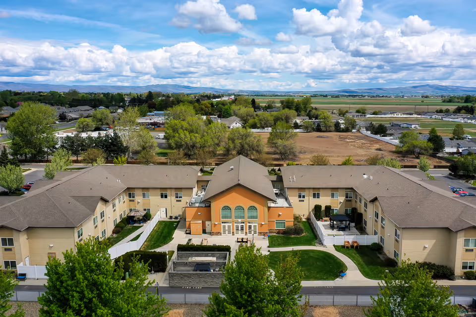 Aerial view of a two-story U-shaped senior living building with a central entrance, courtyard, and surrounding trees and fields.