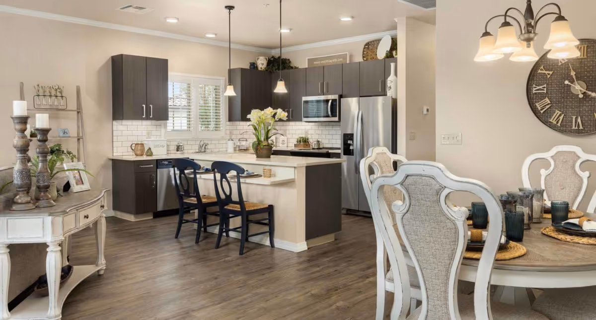 Open-concept kitchen and dining area with a center island, dark cabinets, stainless steel appliances, and a round dining table with chairs.
