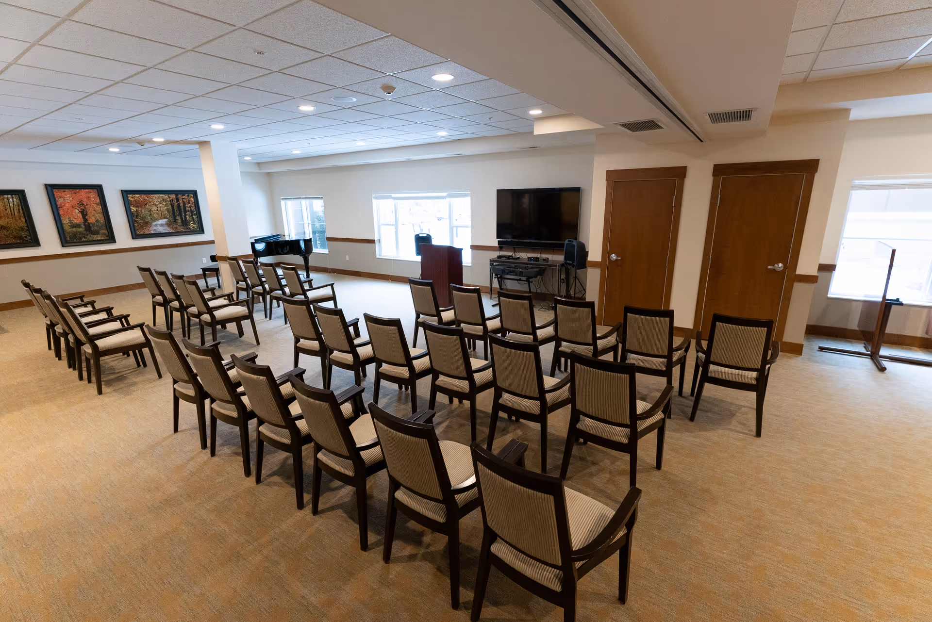 A large multipurpose meeting room with rows of chairs facing a podium, television, and piano.