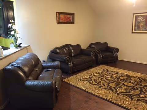 A living room with dark leather couches, a patterned rug, and framed artwork.