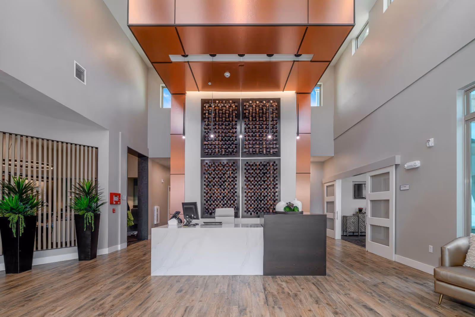 Spacious modern reception lobby with a central marble-front desk, decorative wall art, tall ceilings and potted plants.