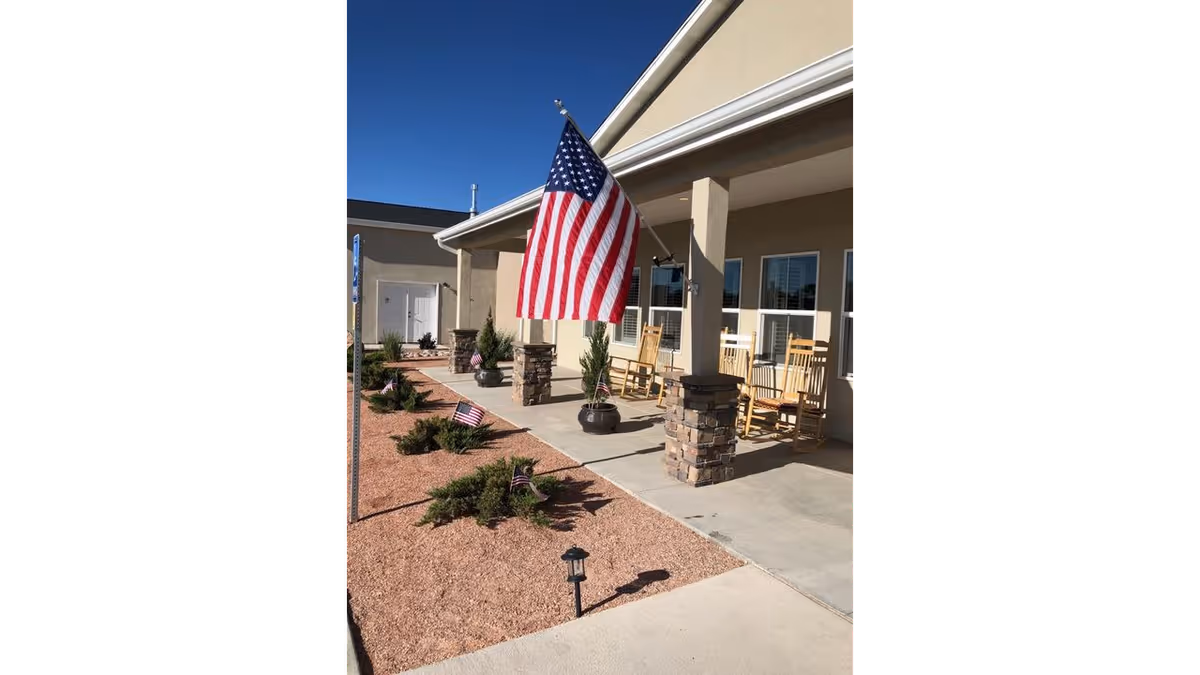 Front porch of a residential facility with an American flag, rocking chairs on a covered patio and gravel landscaping.