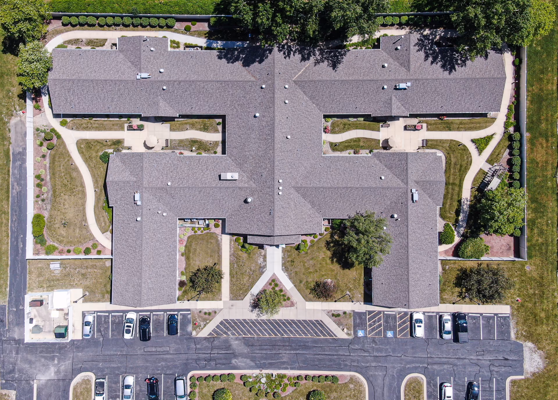 Aerial view of Arden Courts - ProMedica Memory Care Community in South Holland showing the building's roof, surrounding landscaped gardens, pathways, and parking lot with several cars.