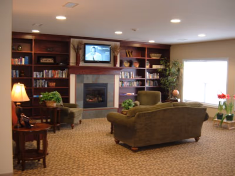 Cozy common room with sofas and armchairs arranged around a fireplace and a wall of bookshelves with a TV above.