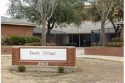 Exterior view of Tandy Village Assisted Living entrance with brick sign and surrounding trees.