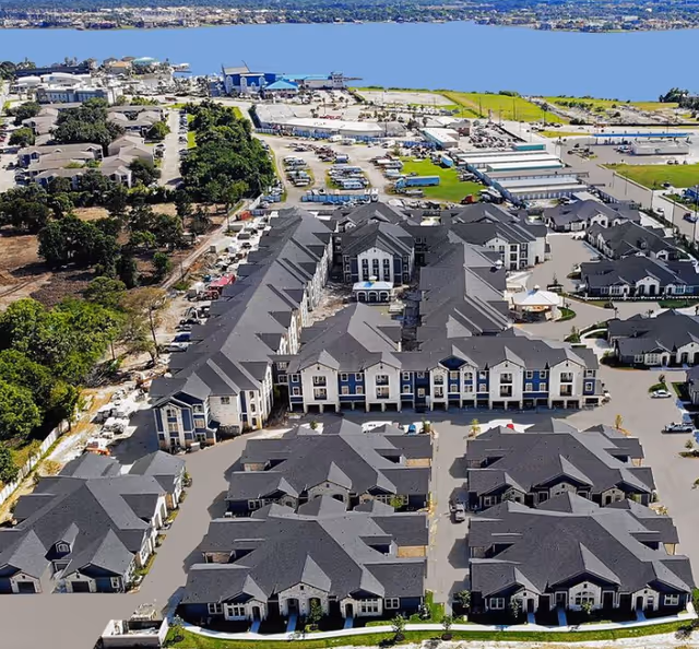 Aerial view of Chesapeake Bay Luxury Active-Adult Community with gray-roofed buildings near water.