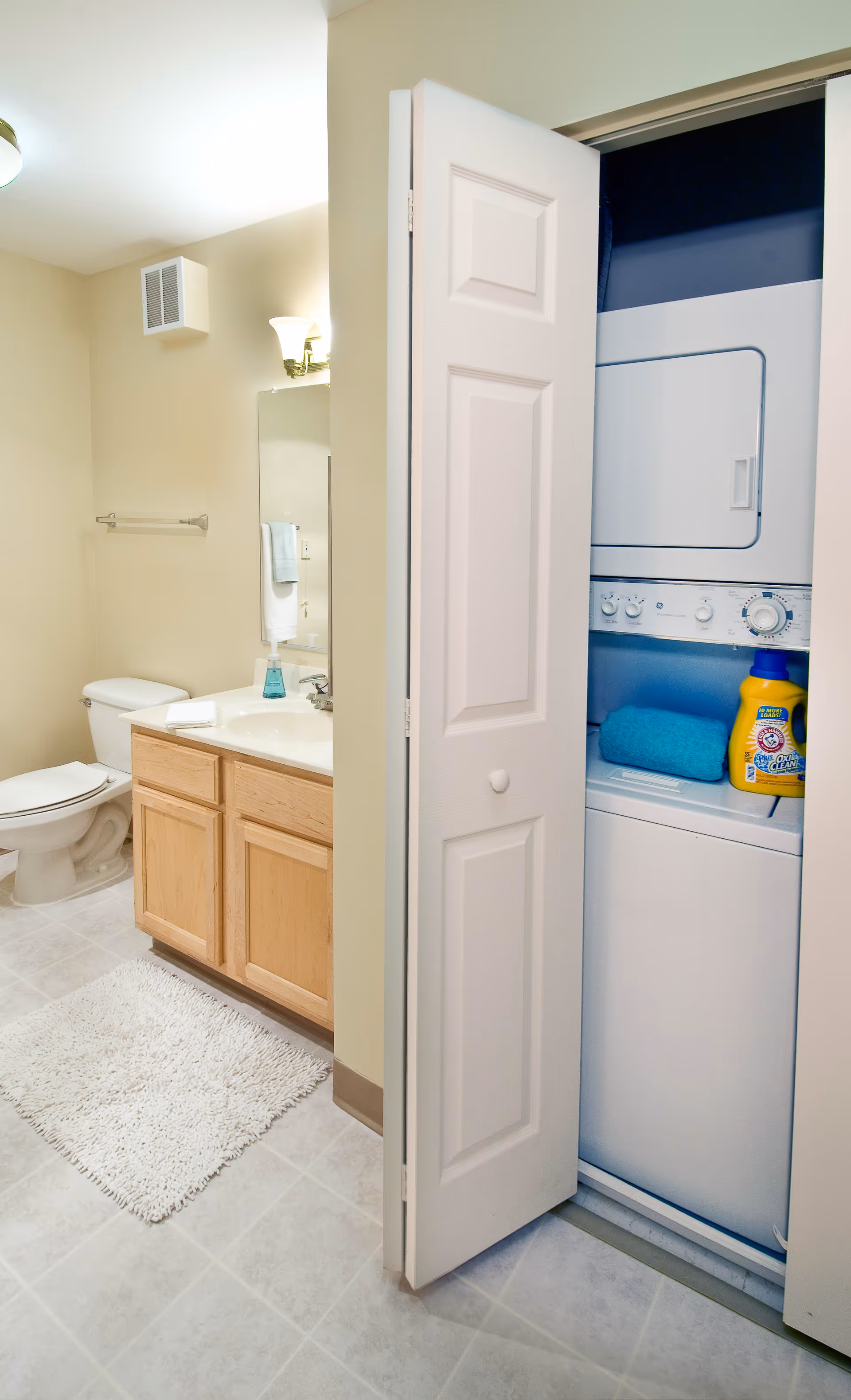 Bathroom with a vanity, toilet, and an open closet containing a stacked washer and dryer.