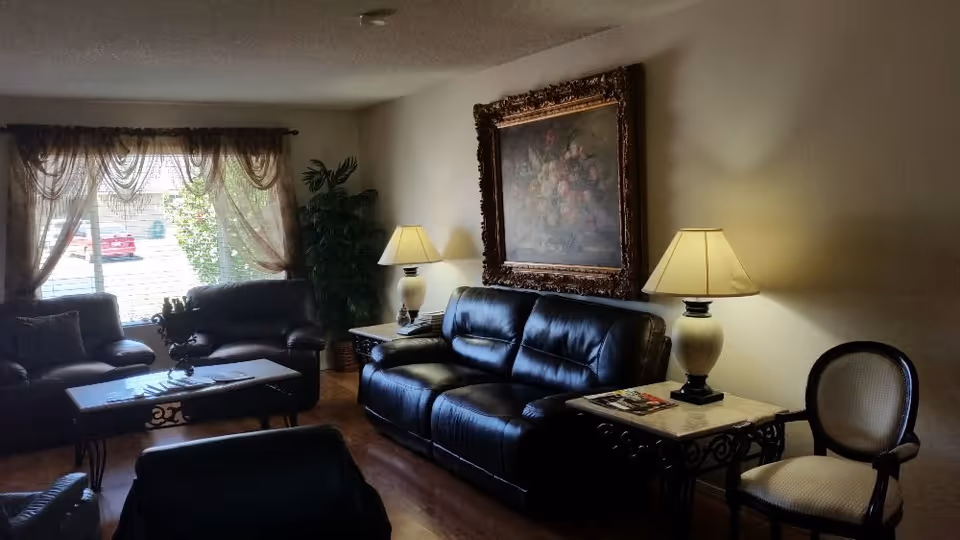 Cozy living room with leather sofas, coffee table, lamps, plant, and large framed painting.