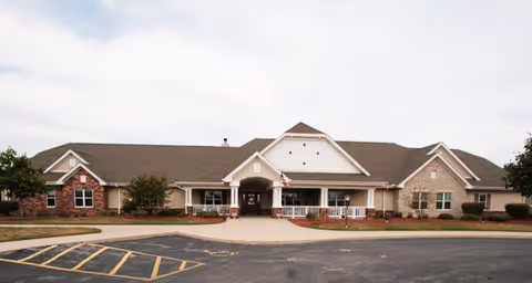 Front exterior of a single-story brick and siding senior living building with a covered porte-cochère entrance and circular driveway.