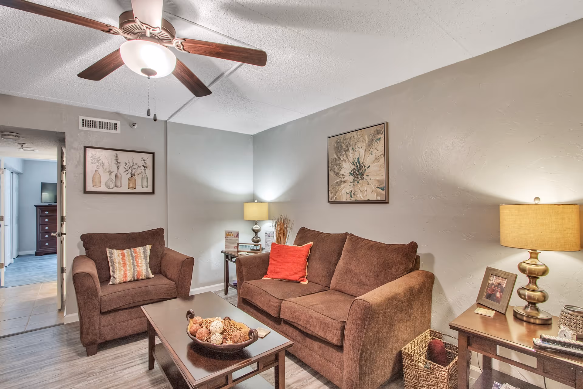 Cozy living room with a brown sofa and armchair, coffee table, ceiling fan, and side lamps.