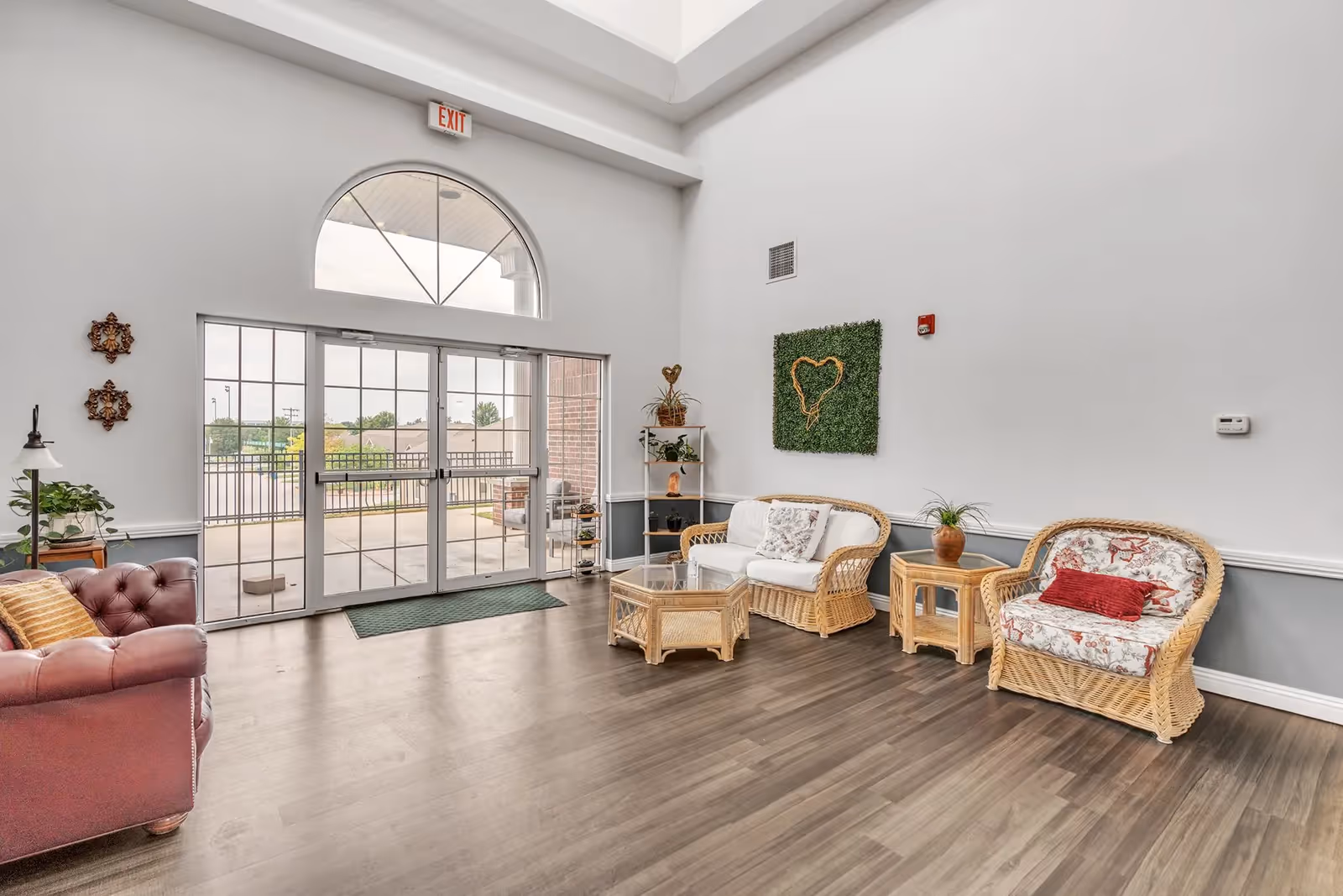 Bright seating area with wicker chairs and a sofa facing large glass entry doors under a high ceiling.