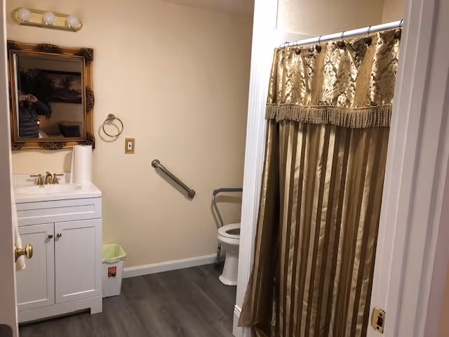 Accessible bathroom with sink, mirror, toilet, grab bars, and striped shower curtain.