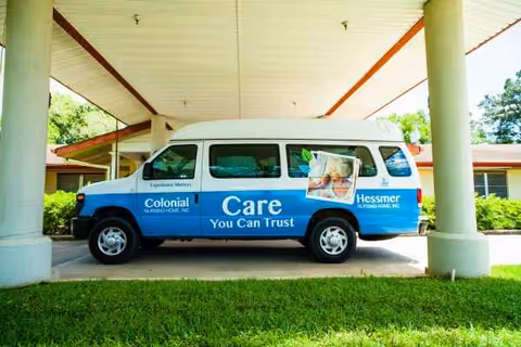 A blue and white Colonial Nursing Home van parked under a covered entrance.