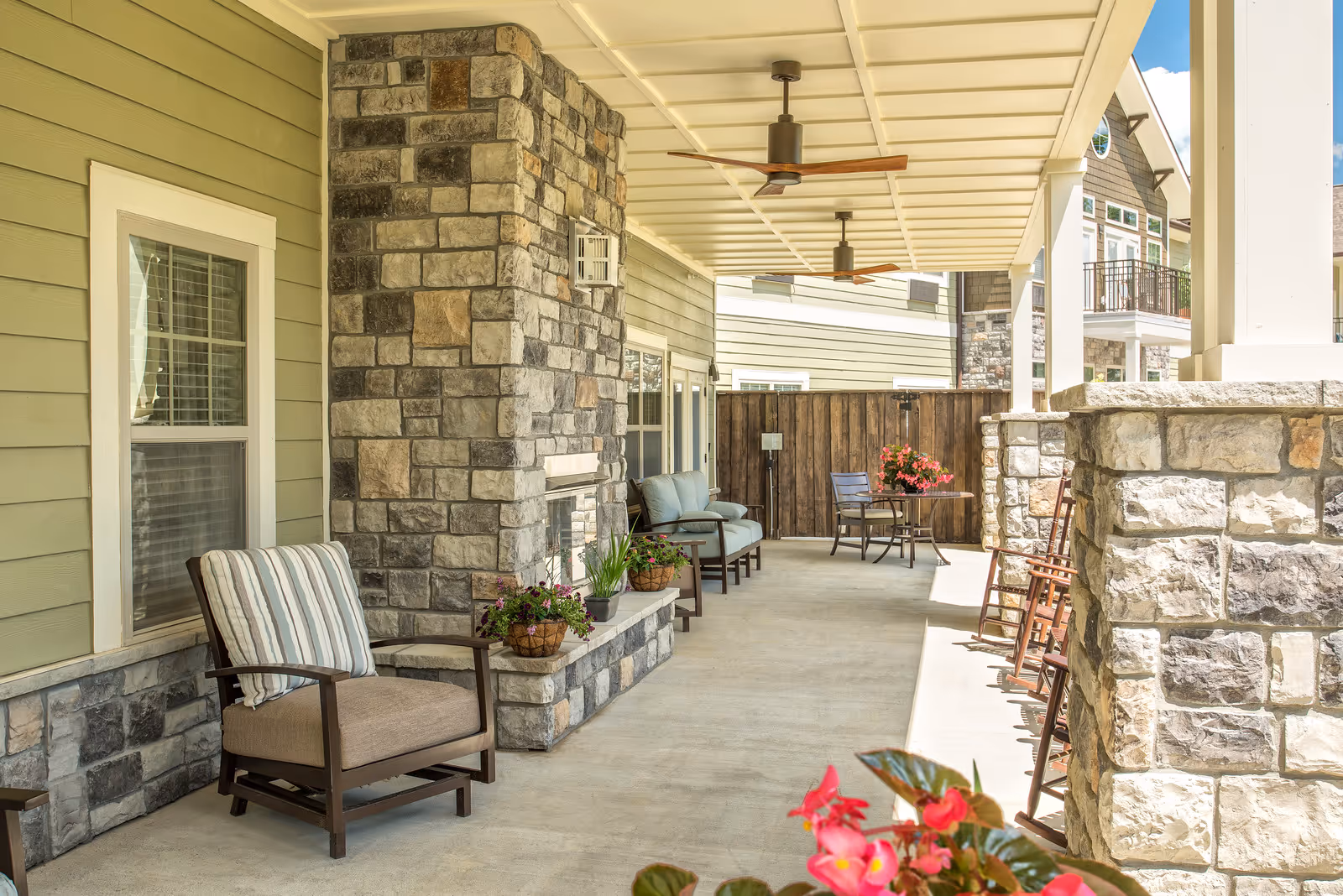 Covered outdoor patio with stone pillars, ceiling fans, comfortable seating and potted plants.