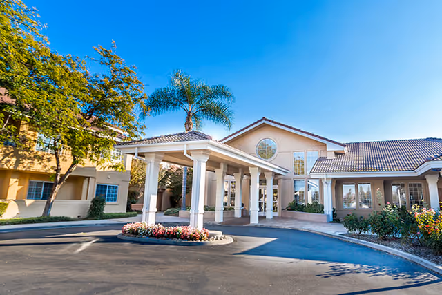 Front entrance of The Chateau at Gardnerville showing a porte-cochere, palm tree, and landscaped driveway under a clear blue sky.