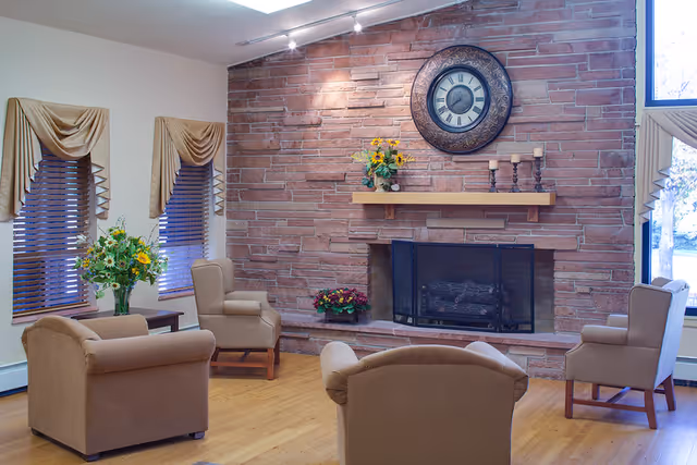 Cozy seating area with armchairs arranged around a stone fireplace topped by a large decorative clock.