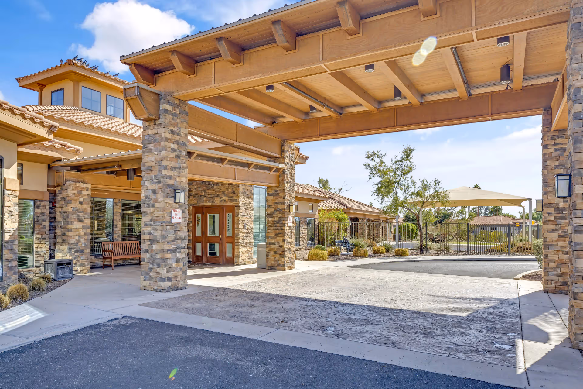 Covered porte-cochere entrance of a stone-clad senior living facility with a driveway and landscaped courtyard.
