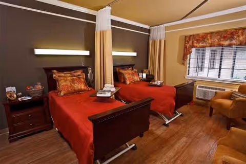 Two twin beds with red bedding and nightstands in a warmly lit resident room.