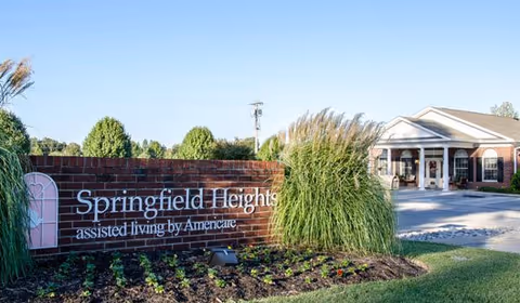 Brick entrance sign reading 'Springfield Heights assisted living by Americare' with landscaping and the facility building visible behind it.