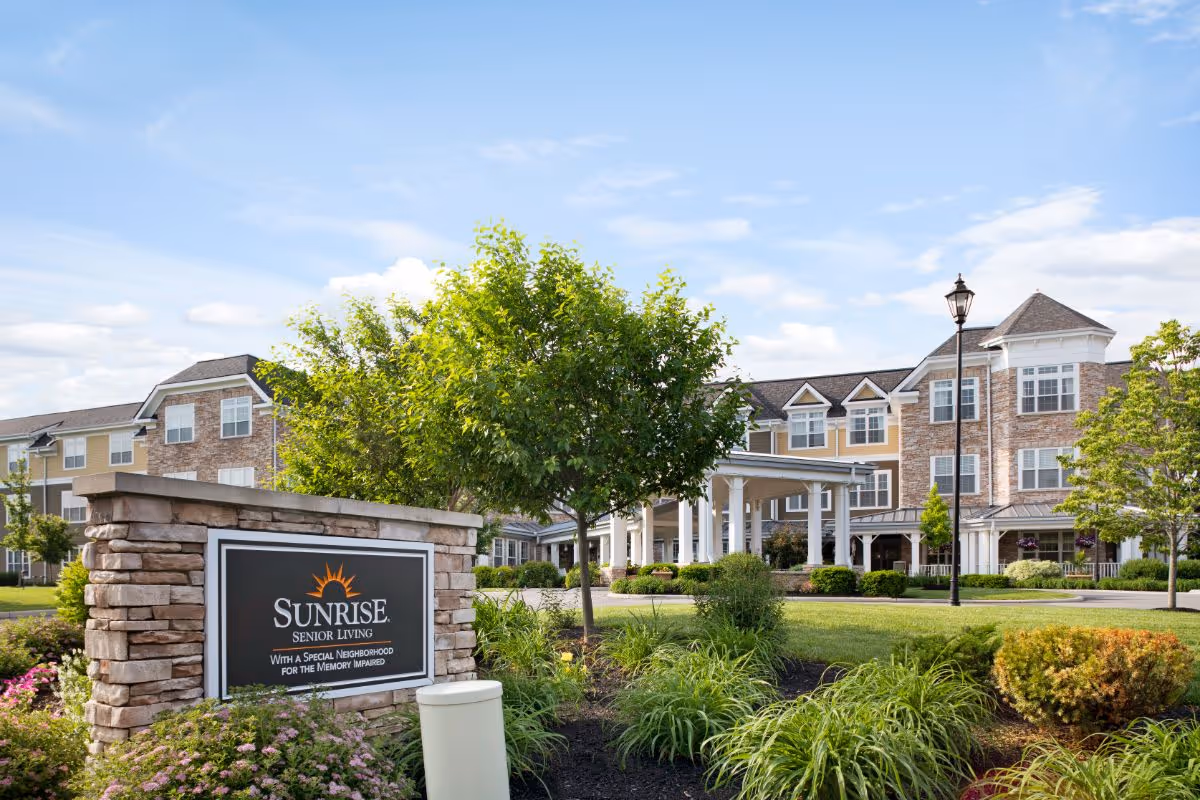 Front entrance and landscaped grounds of the Sunrise senior living facility with a stone sign in the foreground.