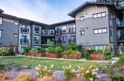 Exterior view of a multi-story senior living building with balconies and landscaped planters.