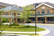 Exterior view of a senior living community building with a covered entrance, landscaped greenery, and a curved driveway.
