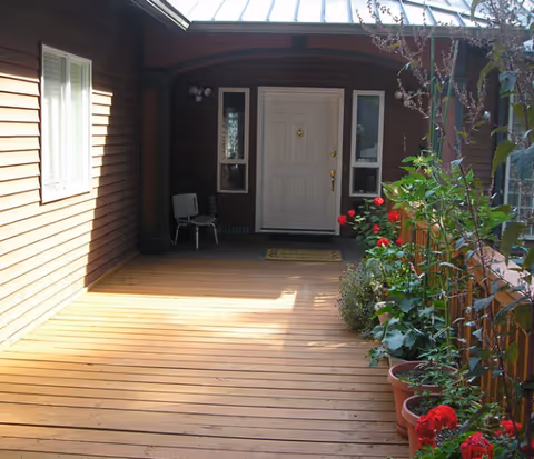 Wooden front porch with potted flowers leads to a white entrance door.