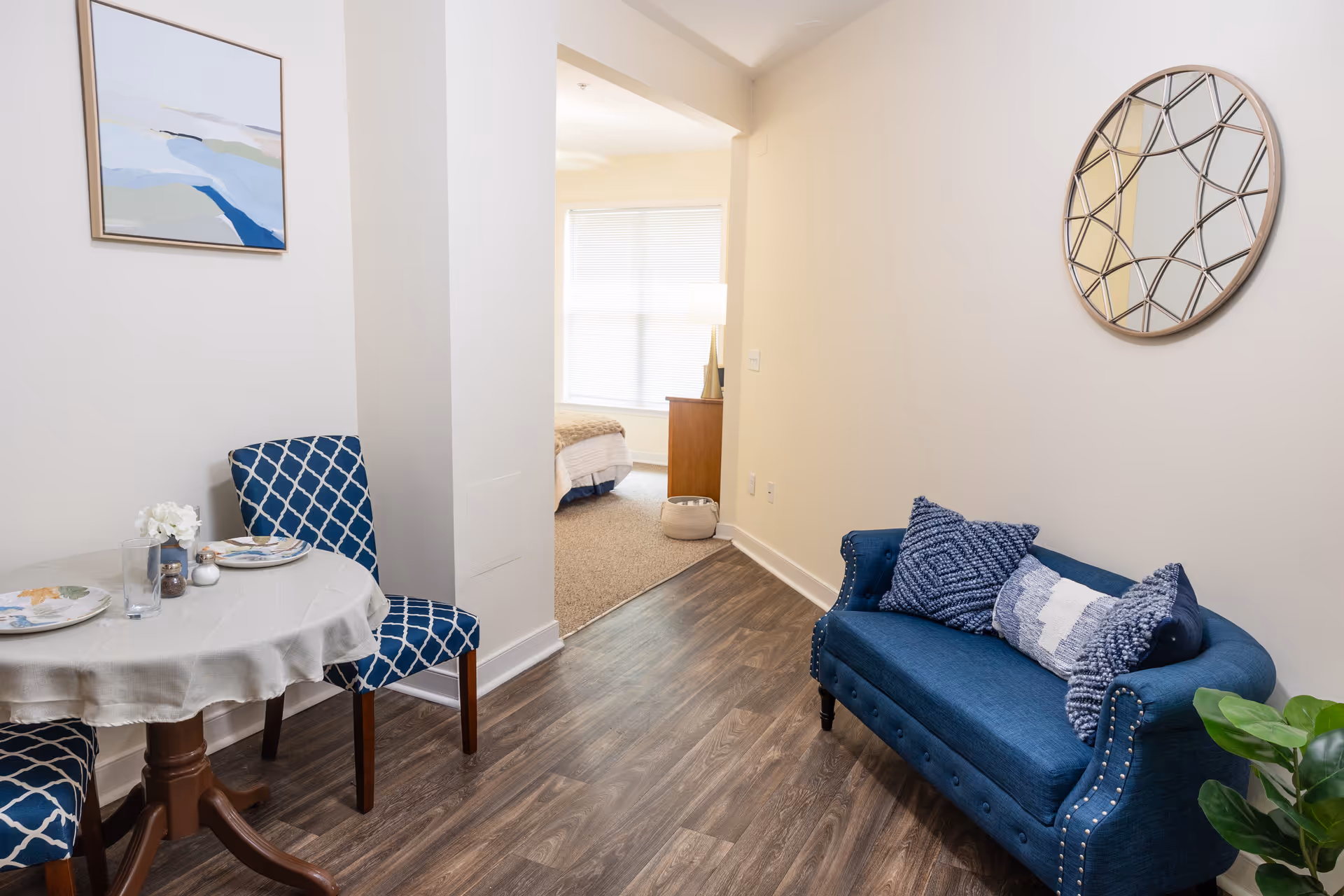 Cozy interior of a senior living lounge with blue sofa, dining table, and wall art.
