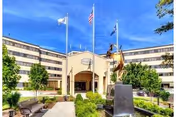 Front entrance of a multi-story senior living building with flags, a sculpture, and a landscaped fountain.
