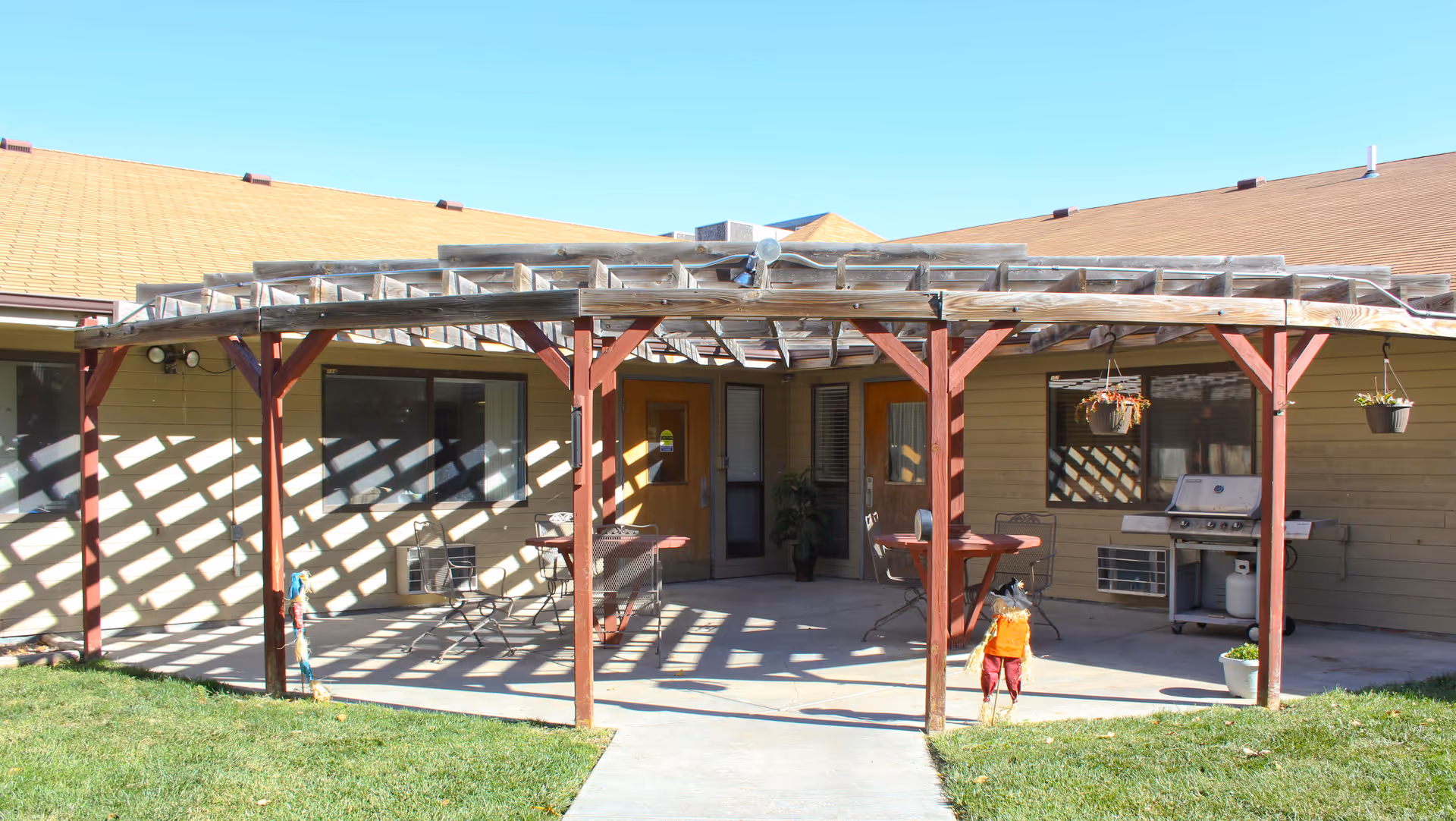 Covered outdoor patio with a wooden pergola, patio furniture and a grill in front of a single-story building.