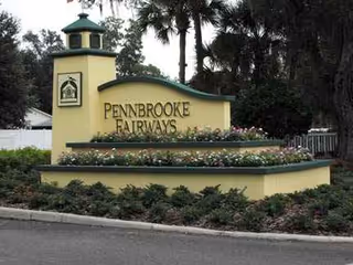 Entrance sign reading Pennbrooke Fairways with landscaped flower beds and tall palm trees.