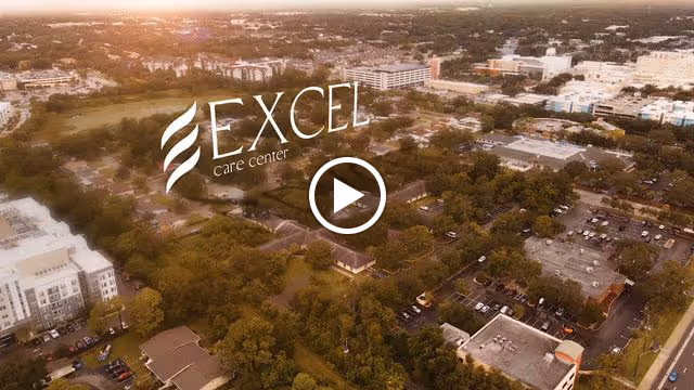 Aerial view of a suburban area with many trees, buildings, and parking lots under a warm, golden sunlight. The image includes the logo and text 'Excel care center' prominently displayed in the center.