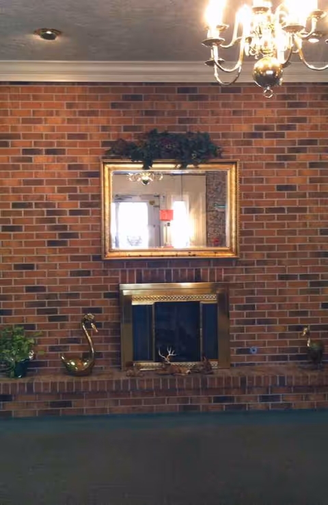 Brick fireplace wall with a gold-framed mirror, decorative items, and a chandelier overhead.