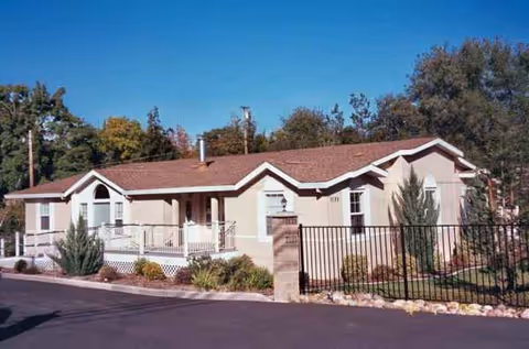 Single-story beige senior living building with a gated entrance and landscaped front yard.