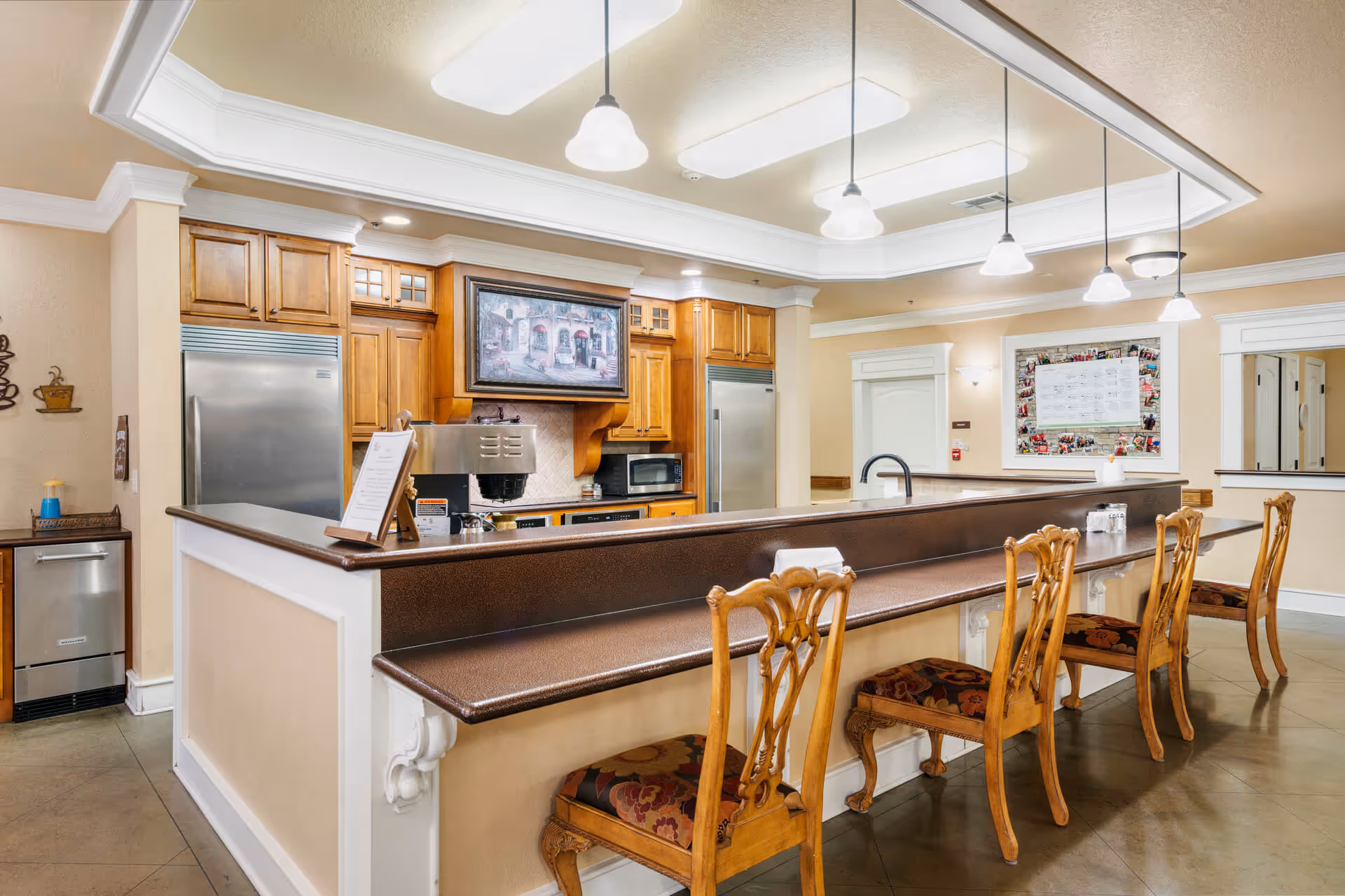 A communal kitchen and serving counter with wooden bar stools, pendant lights, and stainless steel appliances.