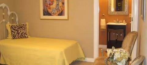 A bright bedroom with a yellow bedspread, zebra pillow, and a bathroom doorway.