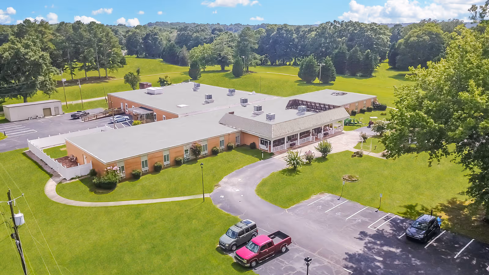 A single-story beige senior living facility with a curved driveway and expansive green lawn.
